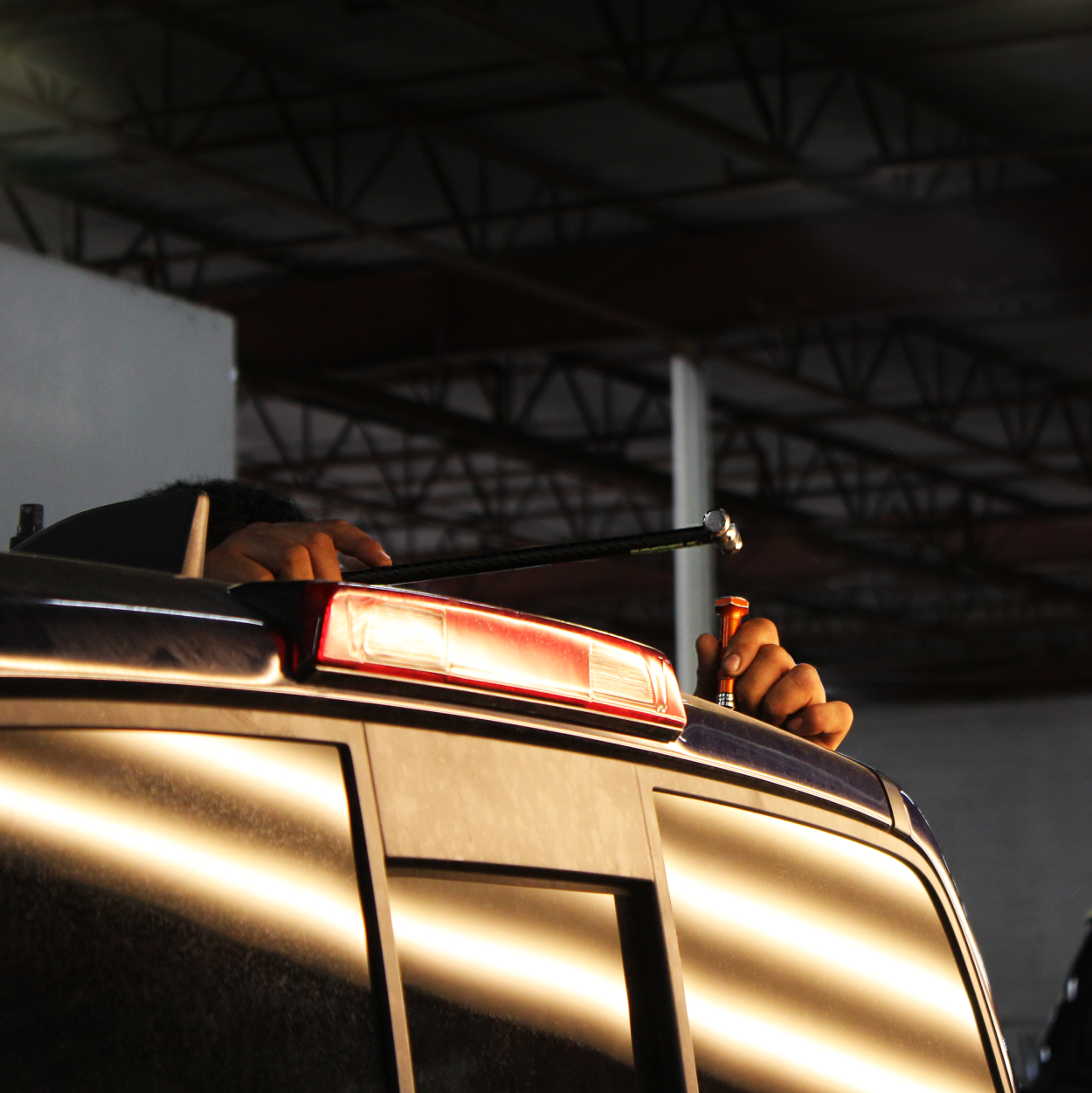 Hands gripping the roof of a vehicle with a red light bar in a dim garage