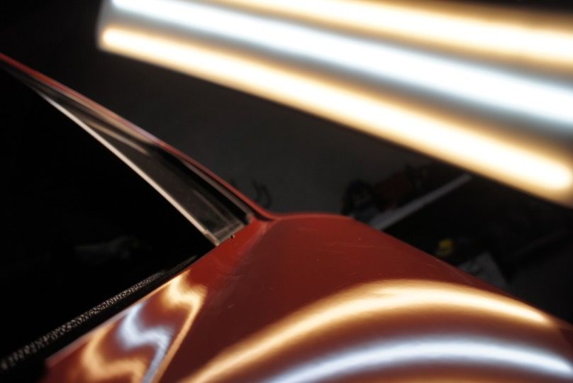 Close-up of a black car door reflecting bright vertical lights at night