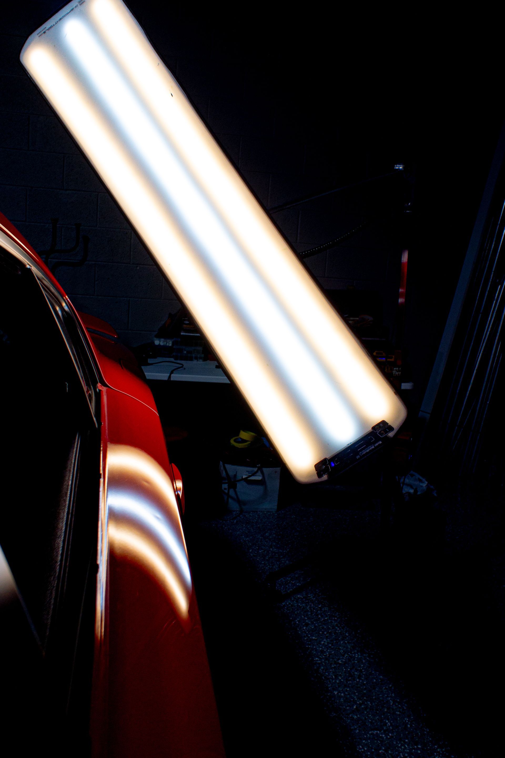 Close-up of a dark blue car fender with bright vertical light reflections and part of a tire visible
