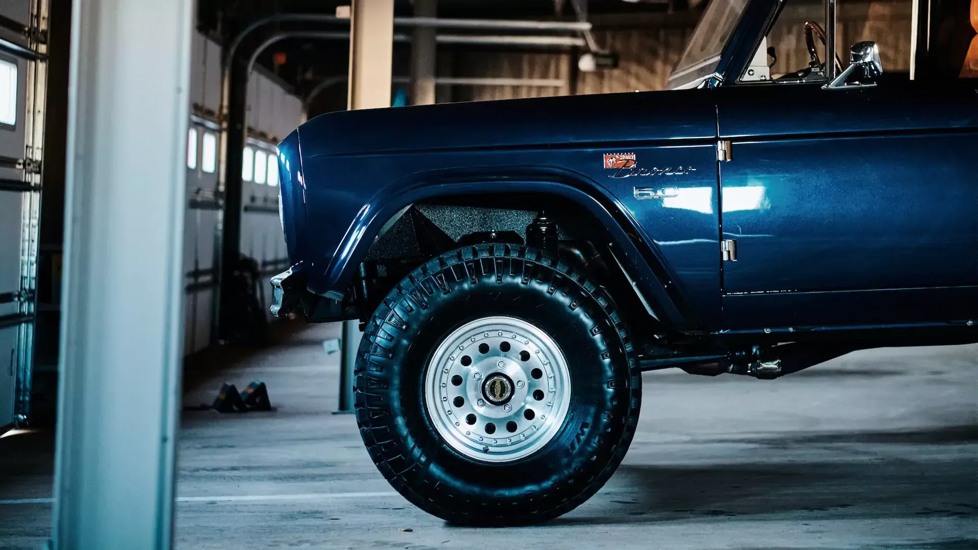 Dark blue classic Ford Bronco with rugged tires in a garage.