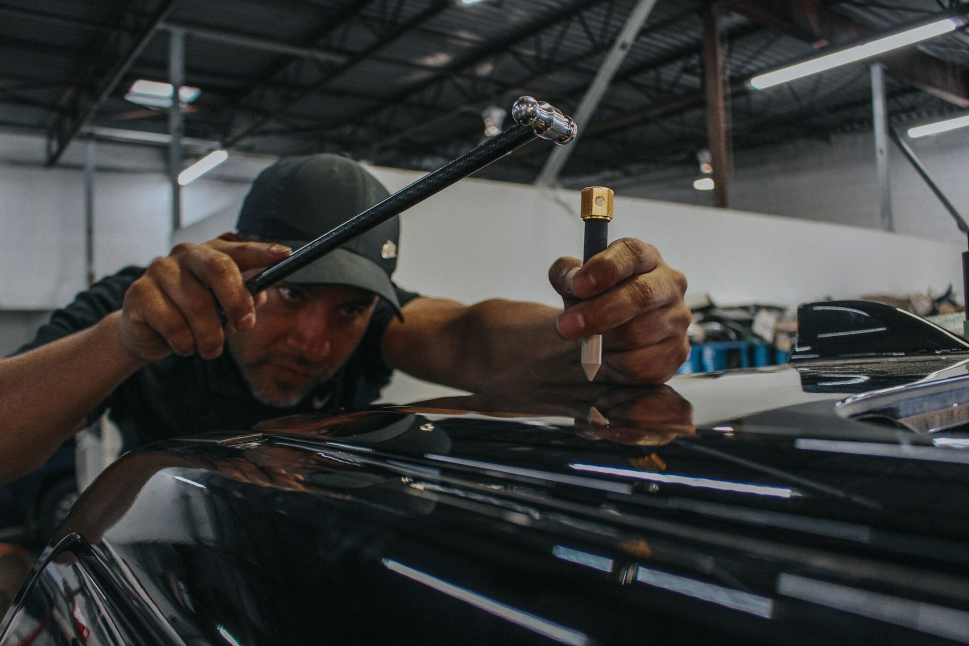 Man using tools to repair a dent on a black car in a workshop.
