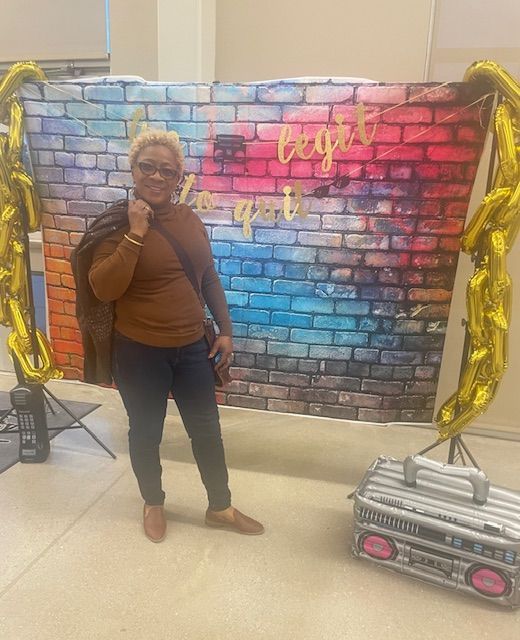 Alice wearing jeans and a brown sweater smiling in front of a colorful festive display.