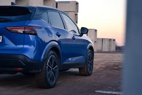 A blue SUV parked outdoors in a dirt lot during sunset, with modern architectural concrete structures in the background.