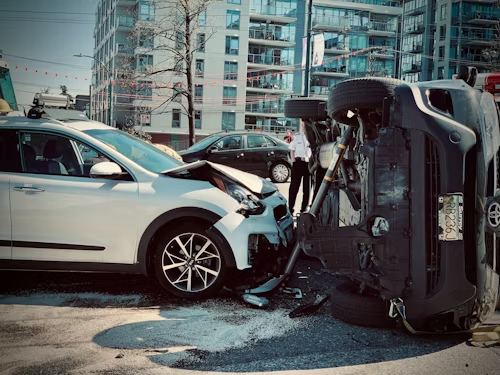 Car accident scene: one car overturned, another damaged; urban setting.