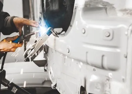 Welder using a torch on a white vehicle, creating sparks in an auto shop.