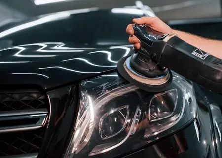 Person using a polisher on a black car's headlight, removing scratches.