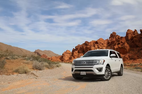 White SUV on a desert road with red rock cliffs and blue sky