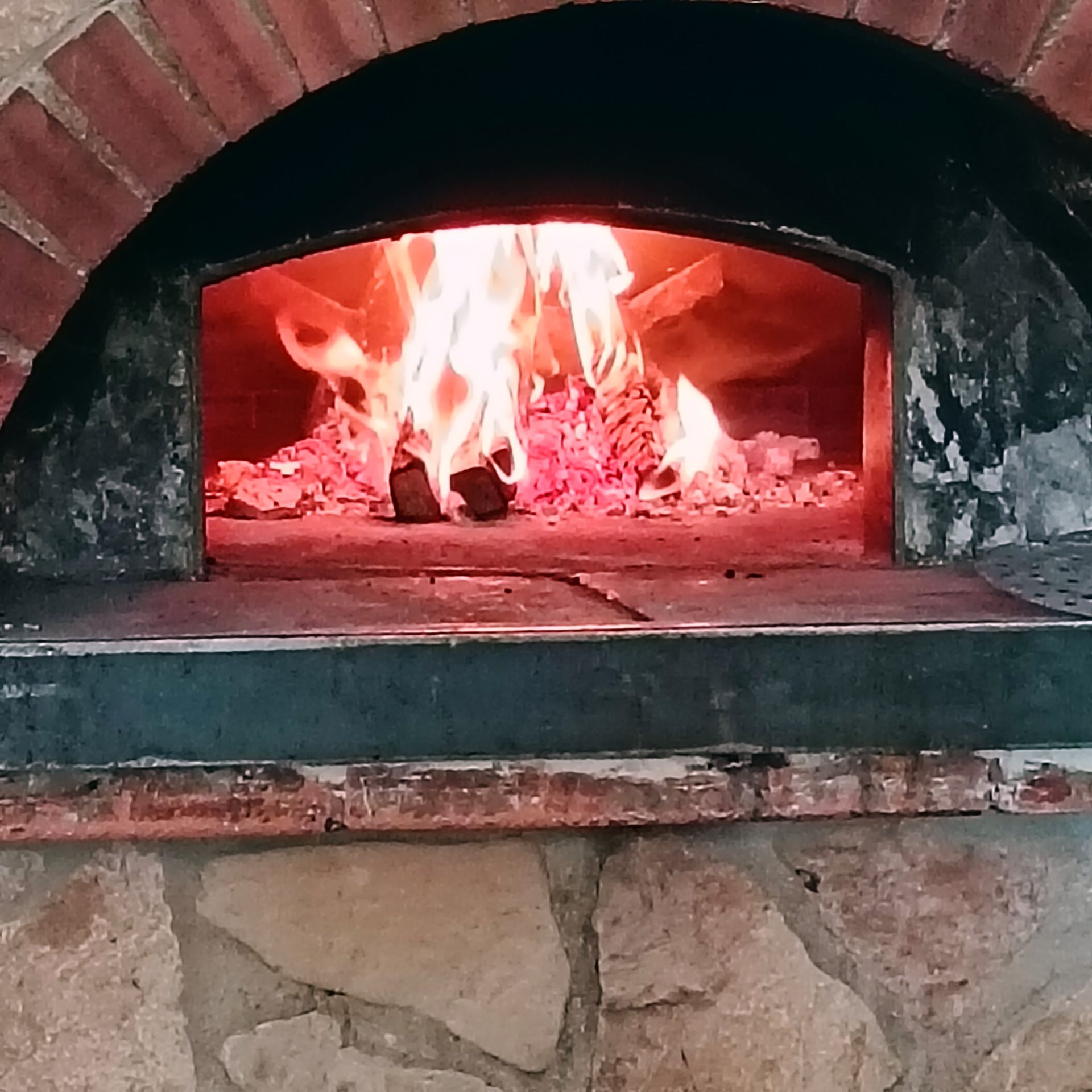 Forno in mattoni a legna con fiamme e braci ardenti all'interno