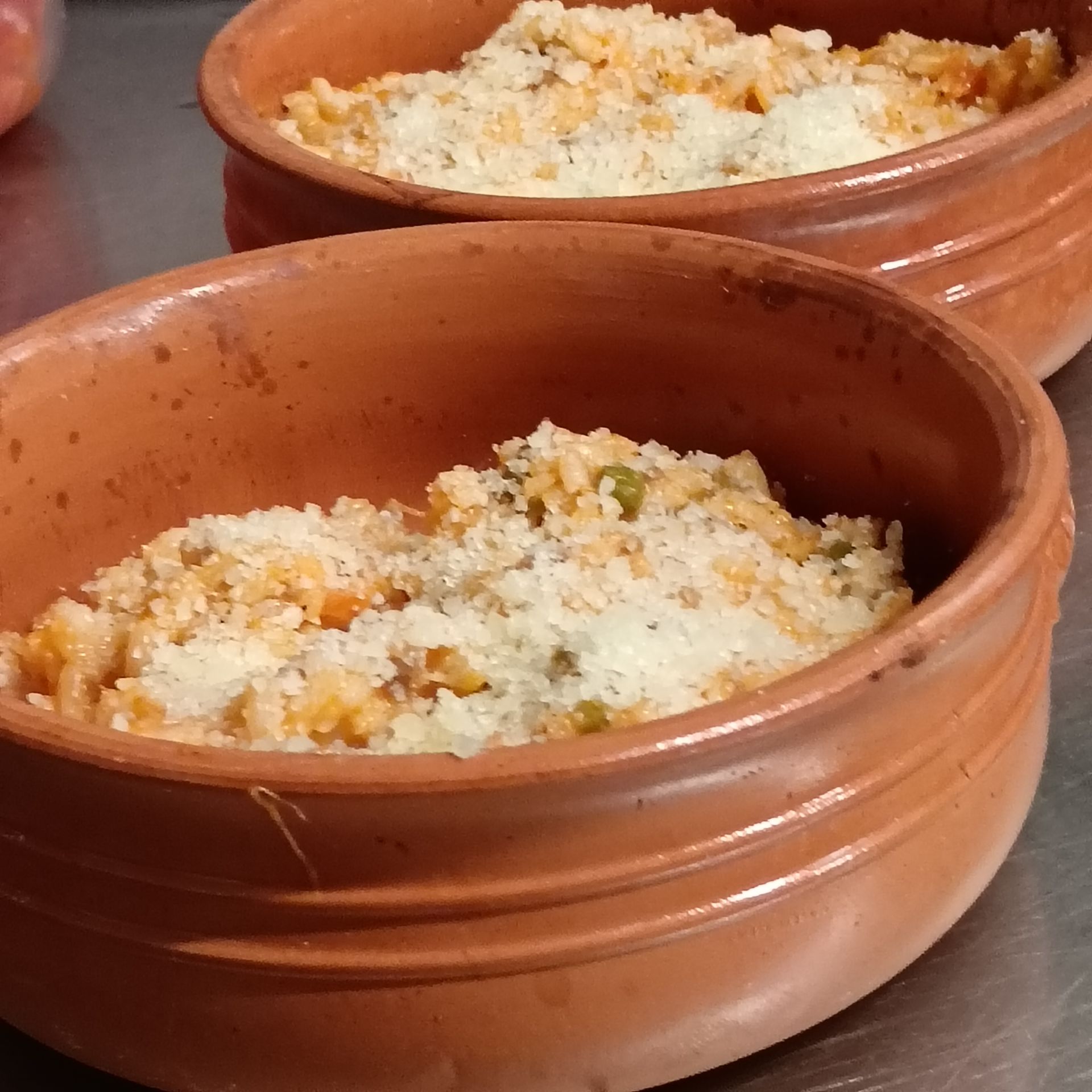 Due ciotole di terracotta piene di riso al forno e verdure su un piano di lavoro
