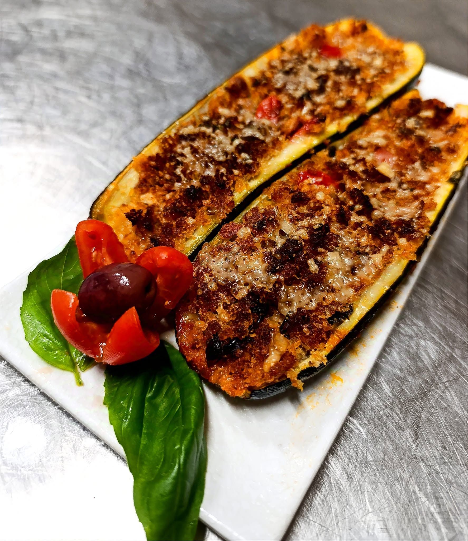 Metà di zucchine grigliate su un piatto bianco con una foglia verde e un pomodorino ciliegino come guarnizione.