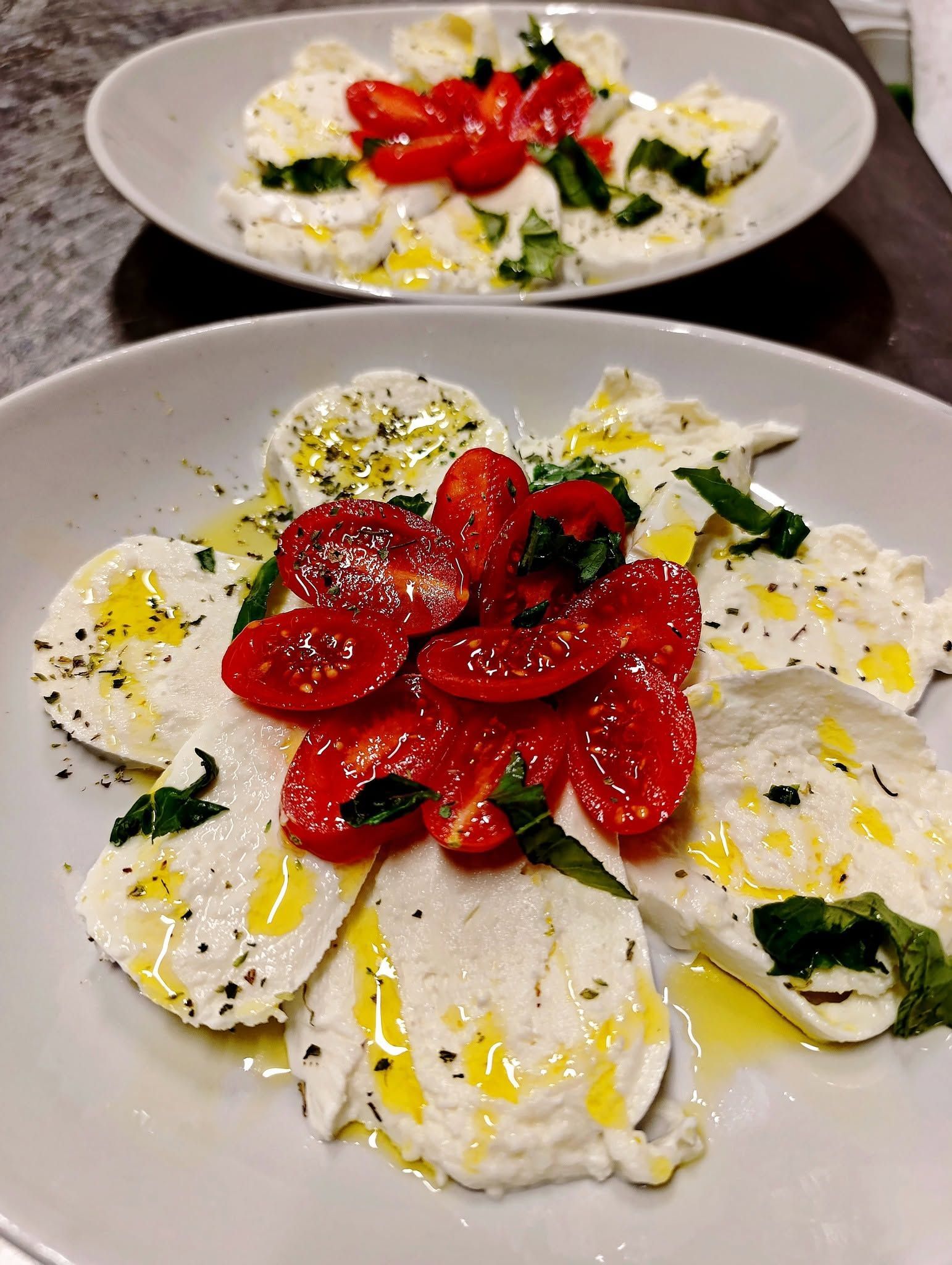 Insalata caprese impiattata con pomodori a fette, mozzarella, basilico e olio d'oliva su un tavolo