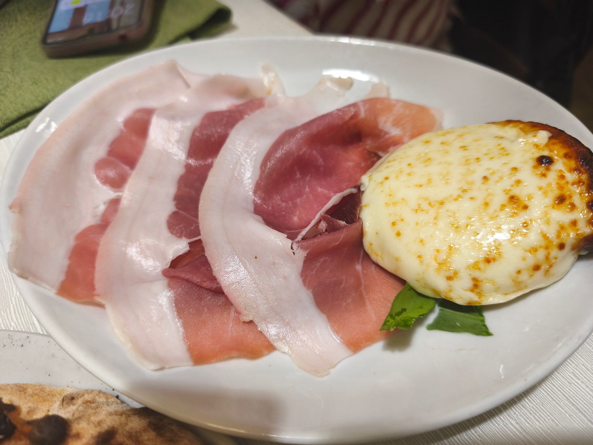 Piatto di prosciutto affettato con un uovo fritto dorato su un piatto bianco.