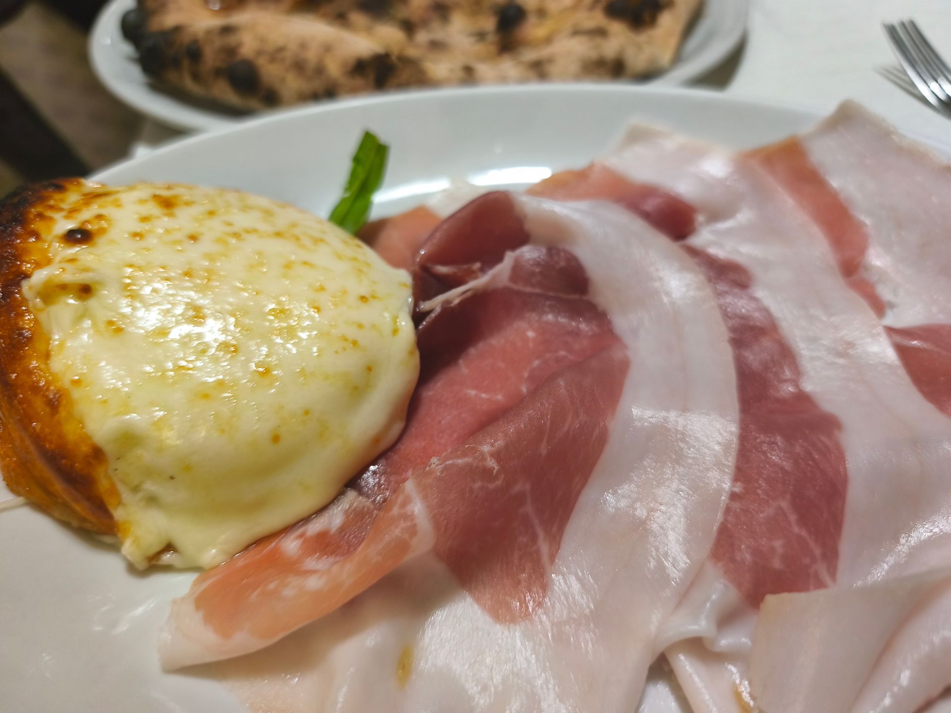 Antipasto al forno con formaggio fuso, servito su un piatto bianco con prosciutto affettato sottilmente.
