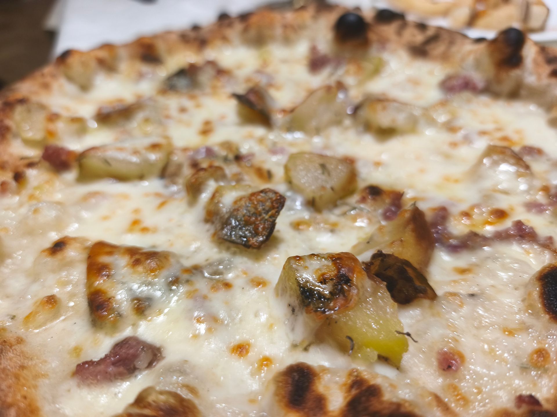 Primo piano di una pizza ricca di formaggio con crosta dorata e funghi sparsi.