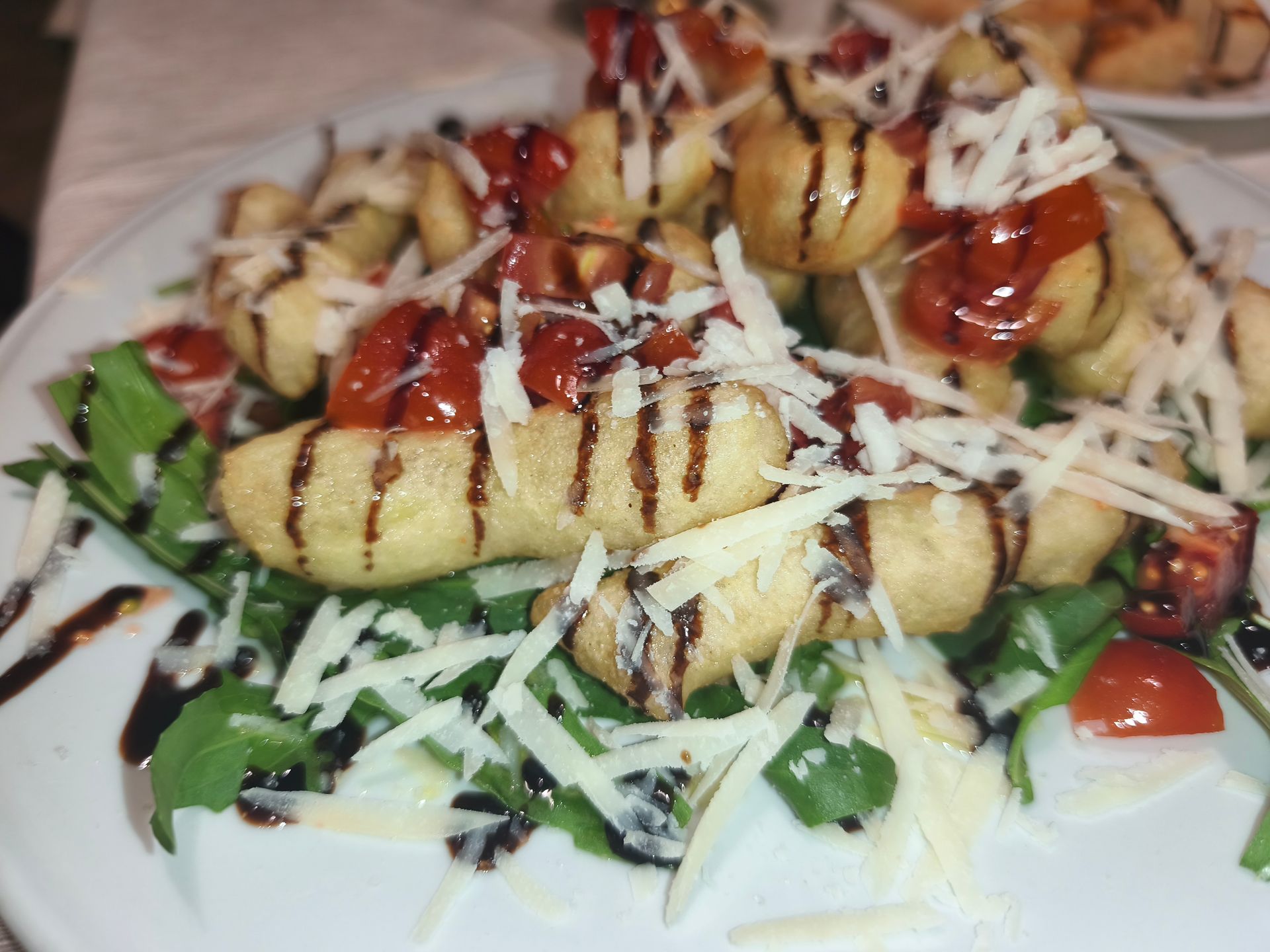 Piatto di verdure grigliate con scaglie di formaggio e salsa a filo, servito su un piatto bianco.