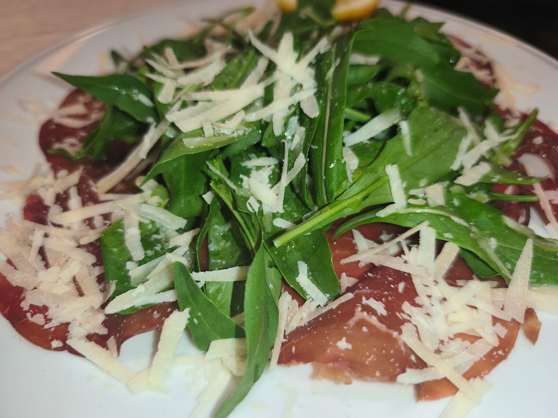 Piatto di insalata con verdure, formaggio grattugiato e pomodori a fette su un piatto bianco.