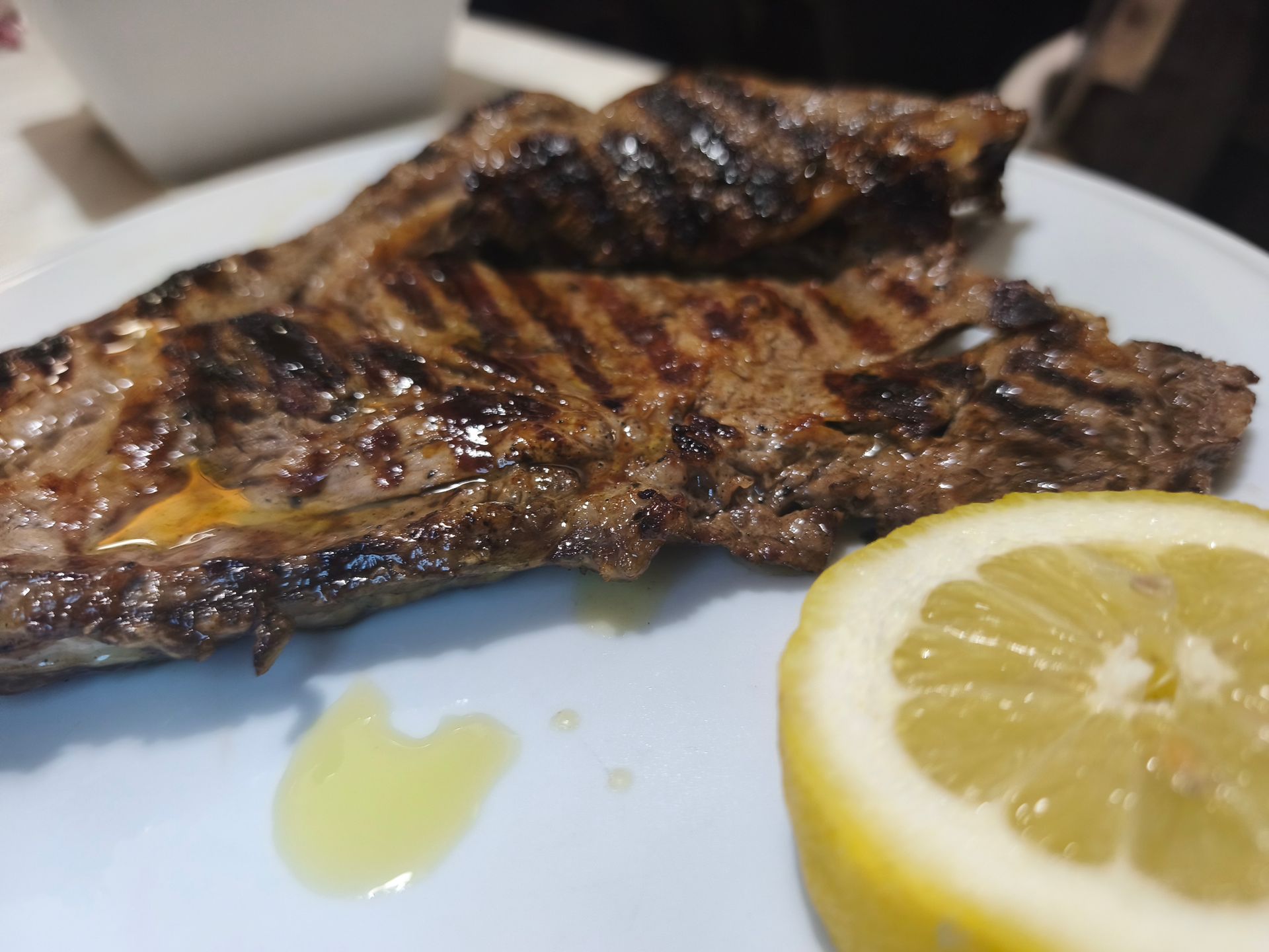 Filetto di pesce grigliato su un piatto bianco con spicchi di limone e un filo d'olio.