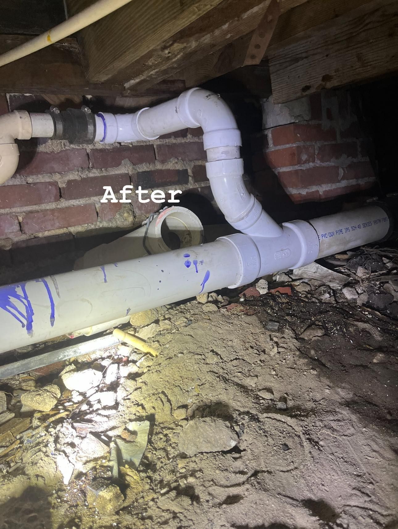 After photo of white PVC pipes under a crawlspace, showing a new elbow and branch connection.