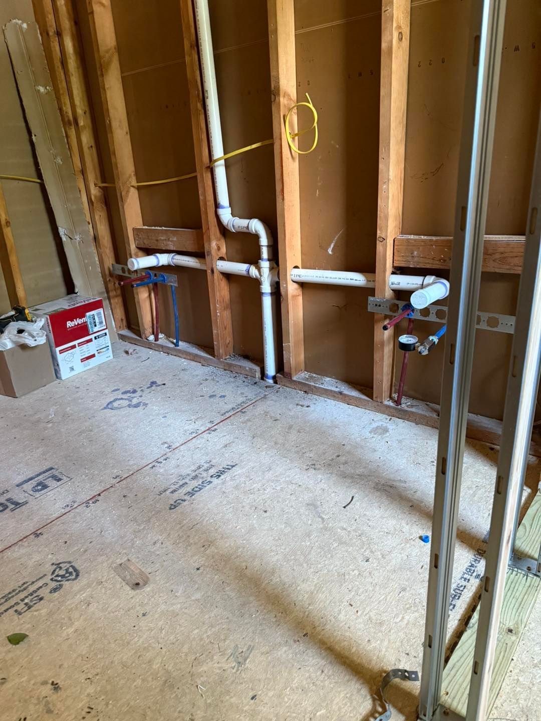 Unfinished room with exposed wall studs, plumbing pipes, and subflooring during construction