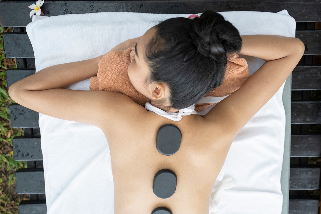 A person lying face down on a massage table receiving a hot stone treatment on their back. A person lying face down on a massage table receiving a hot stone treatment on their back.