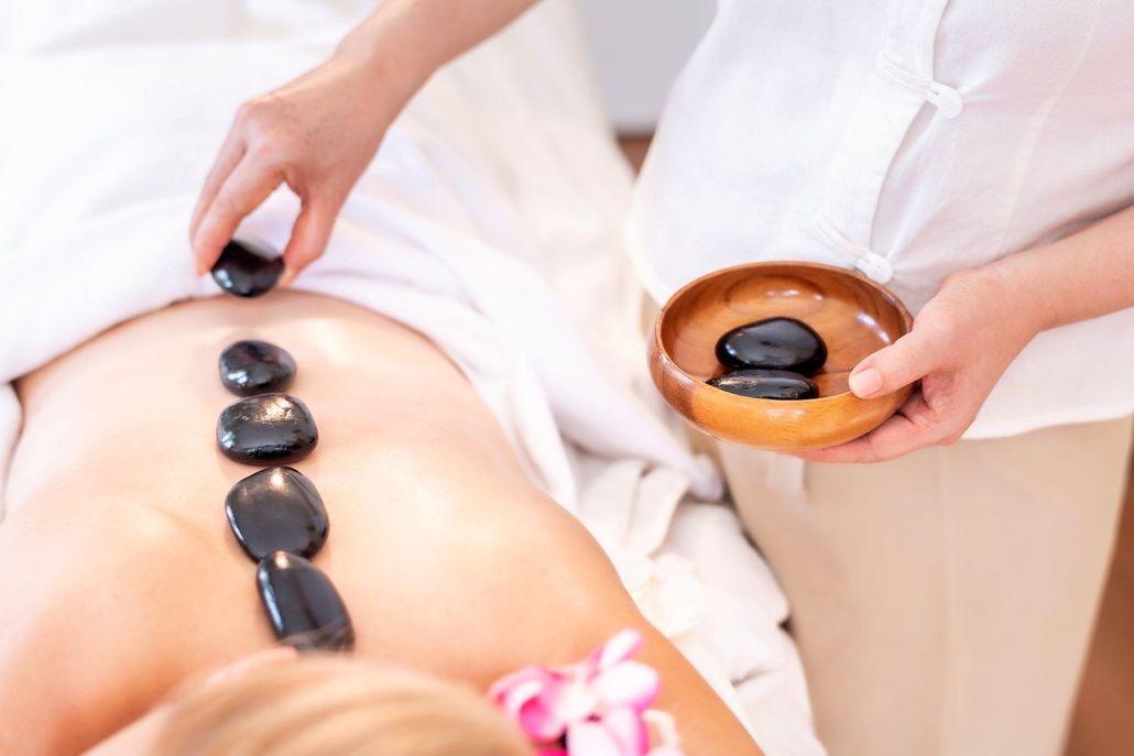 A therapist places smooth, dark heated stones along a client’s back during a professional spa treatment. A therapist places smooth, dark heated stones along a client’s back during a professional spa treatment.