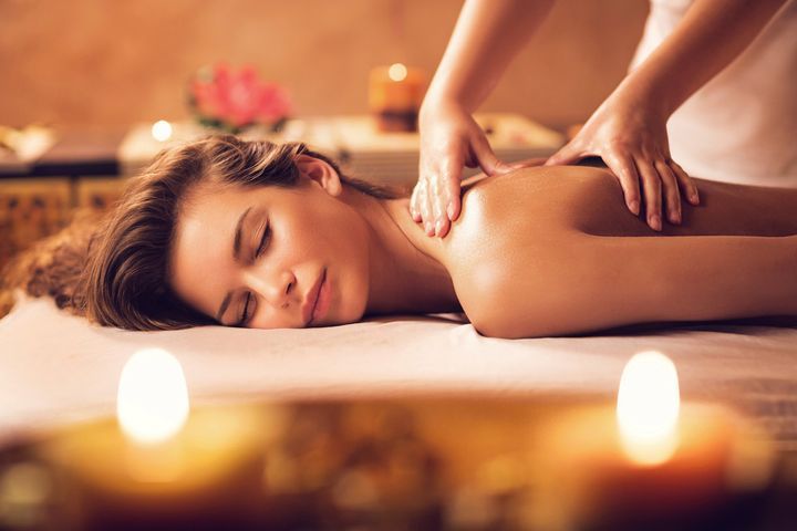 A person receives a relaxing back massage in a spa, with soft, blurred candlelight in the foreground.