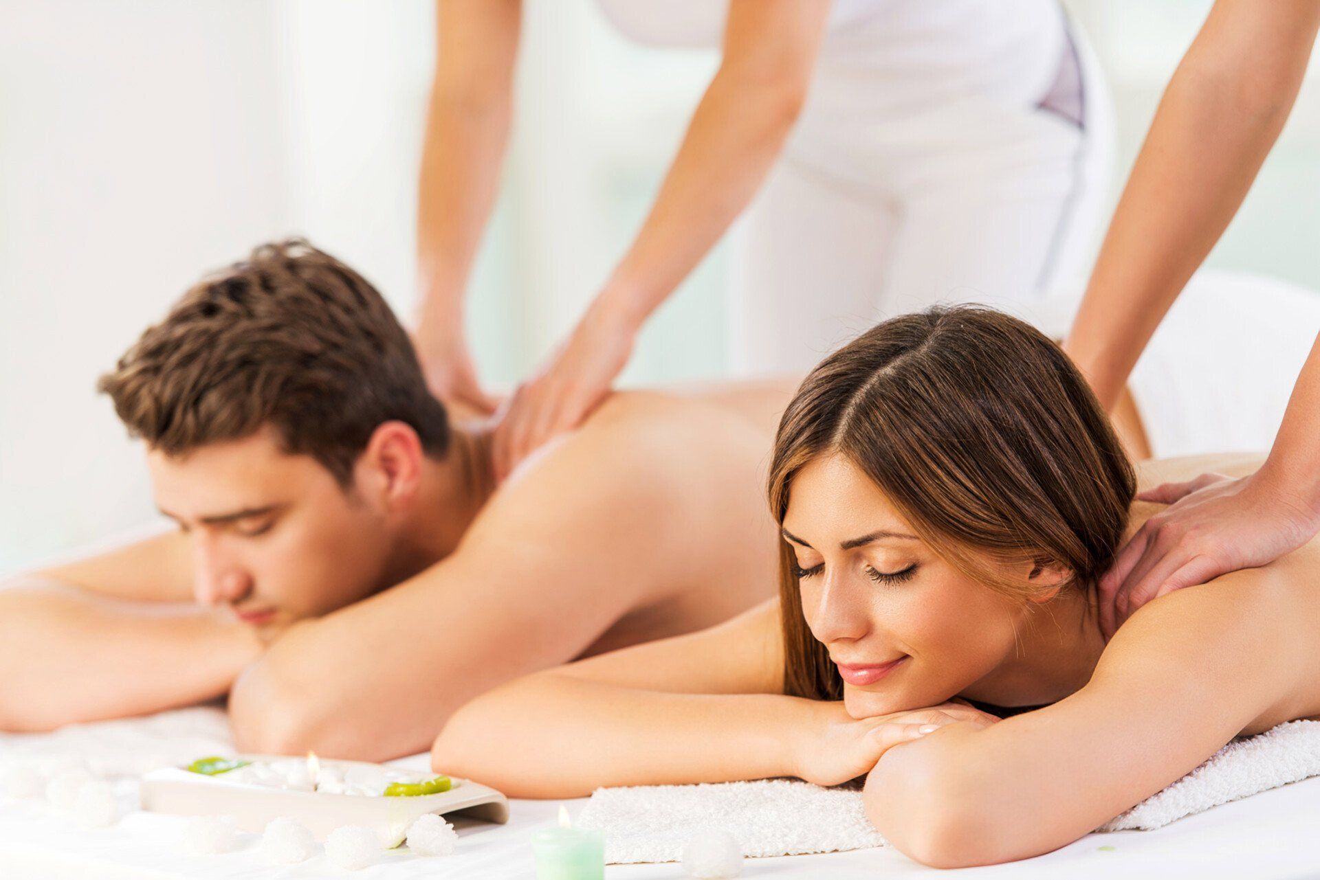 A couple relaxing on massage tables while receiving shoulder massages in a spa setting. A couple relaxing on massage tables while receiving shoulder massages in a spa setting.