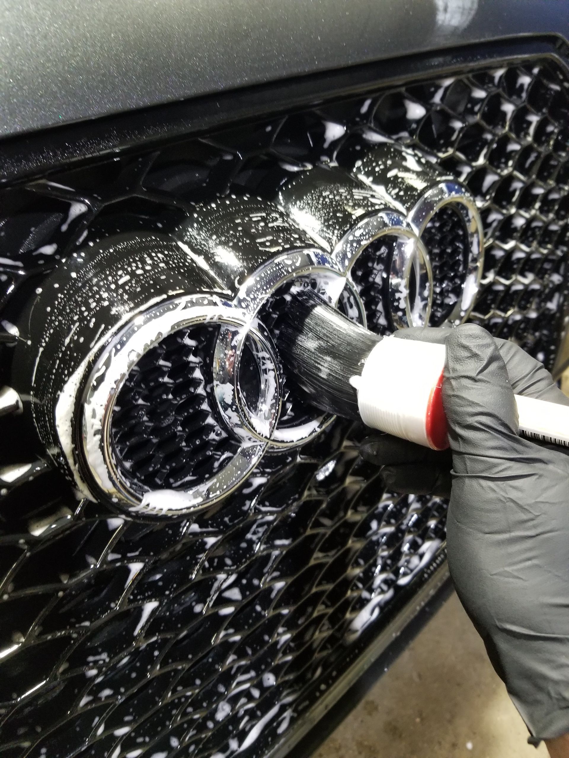 A man is cleaning the wheel of a black car with a sponge.