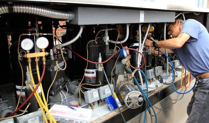 Technician inspecting exposed machinery with gauges, hoses, and wiring in a cluttered equipment compartment