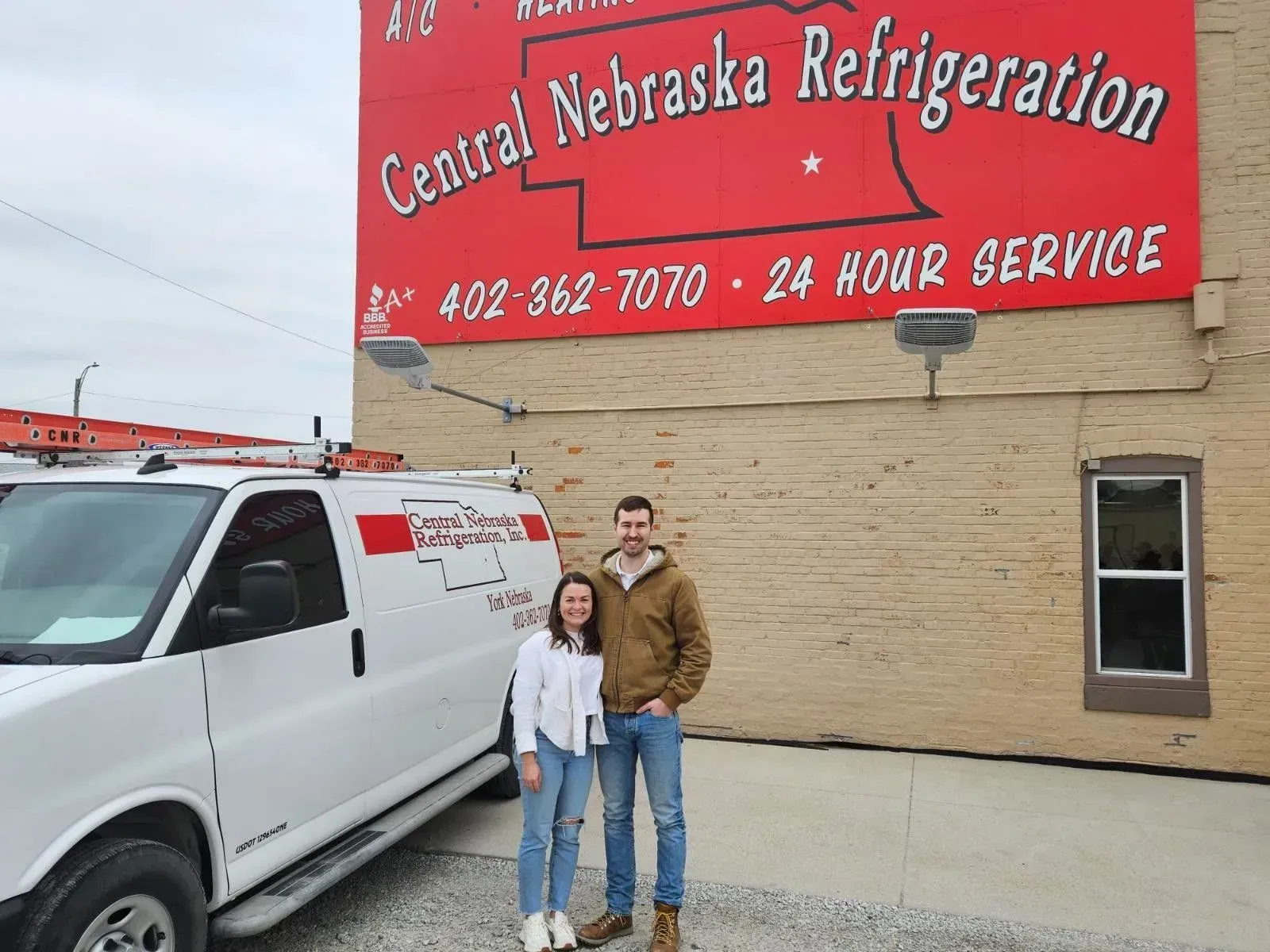 Two people standing beside a white service van in front of Central Nebraska Refrigeration building
