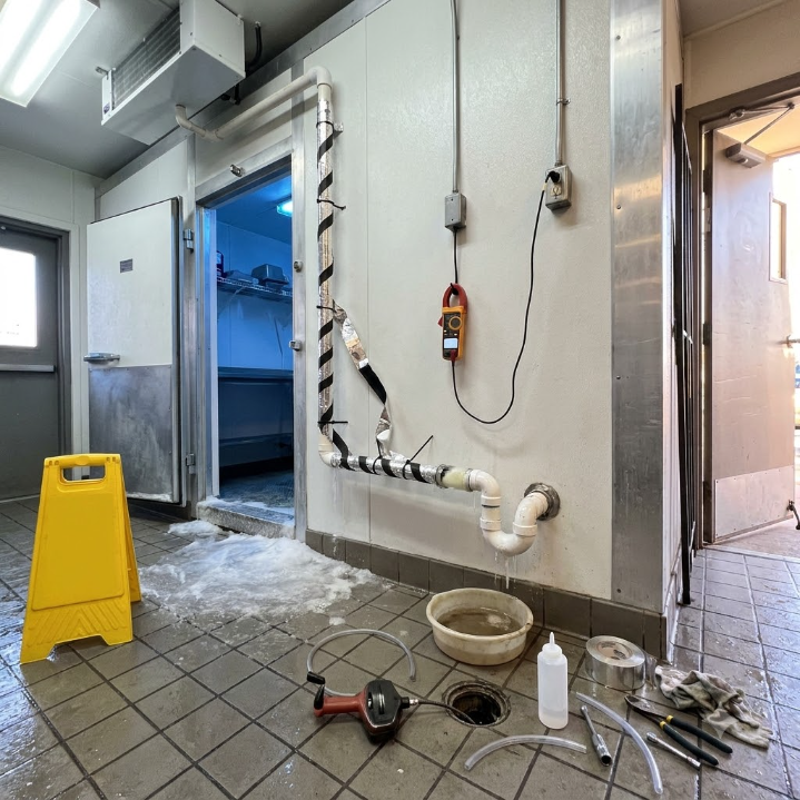 Person using a handheld meter to inspect a water heater and nearby pipes in a utility room