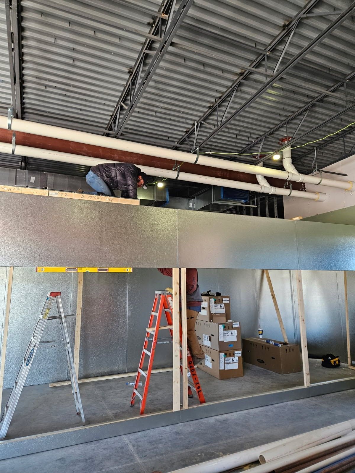 Warehouse interior with two workers on a catwalk above ladders and stacked boxes below