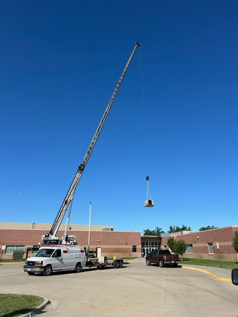 Two cranes lifting equipment in a parking lot beside a brick building under a clear blue sky
