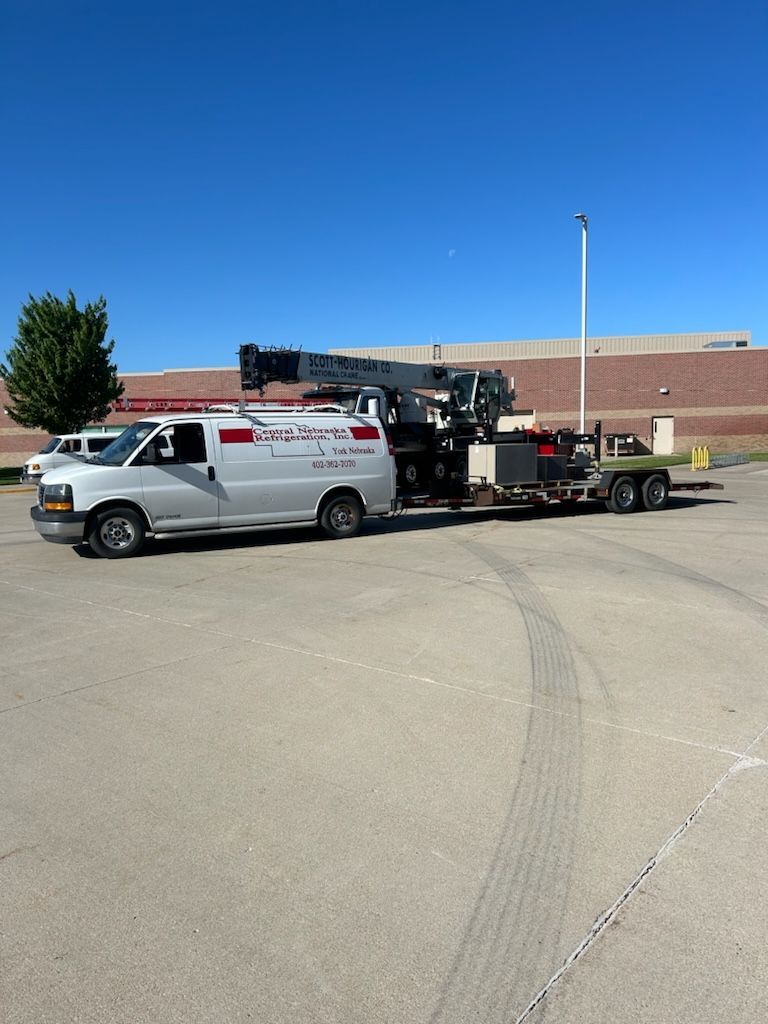 White utility van towing a black equipment trailer in a parking lot under a clear blue sky