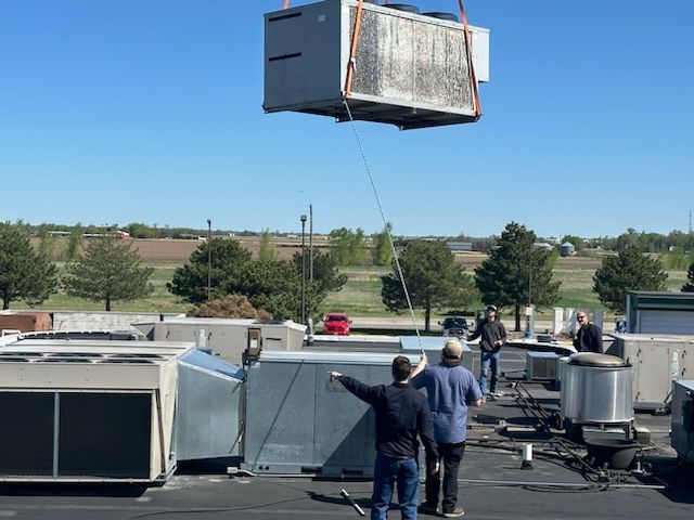Workers lifting a rooftop HVAC unit by crane over a commercial building