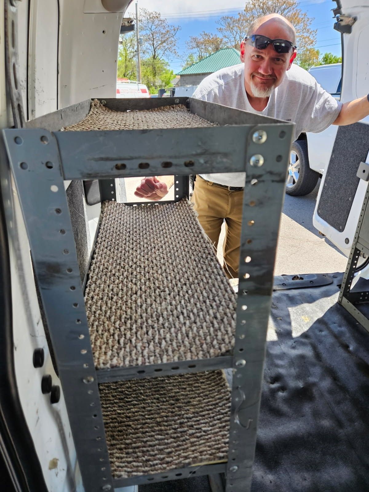 Man in sunglasses pushing a metal rack out of a van in bright daylight