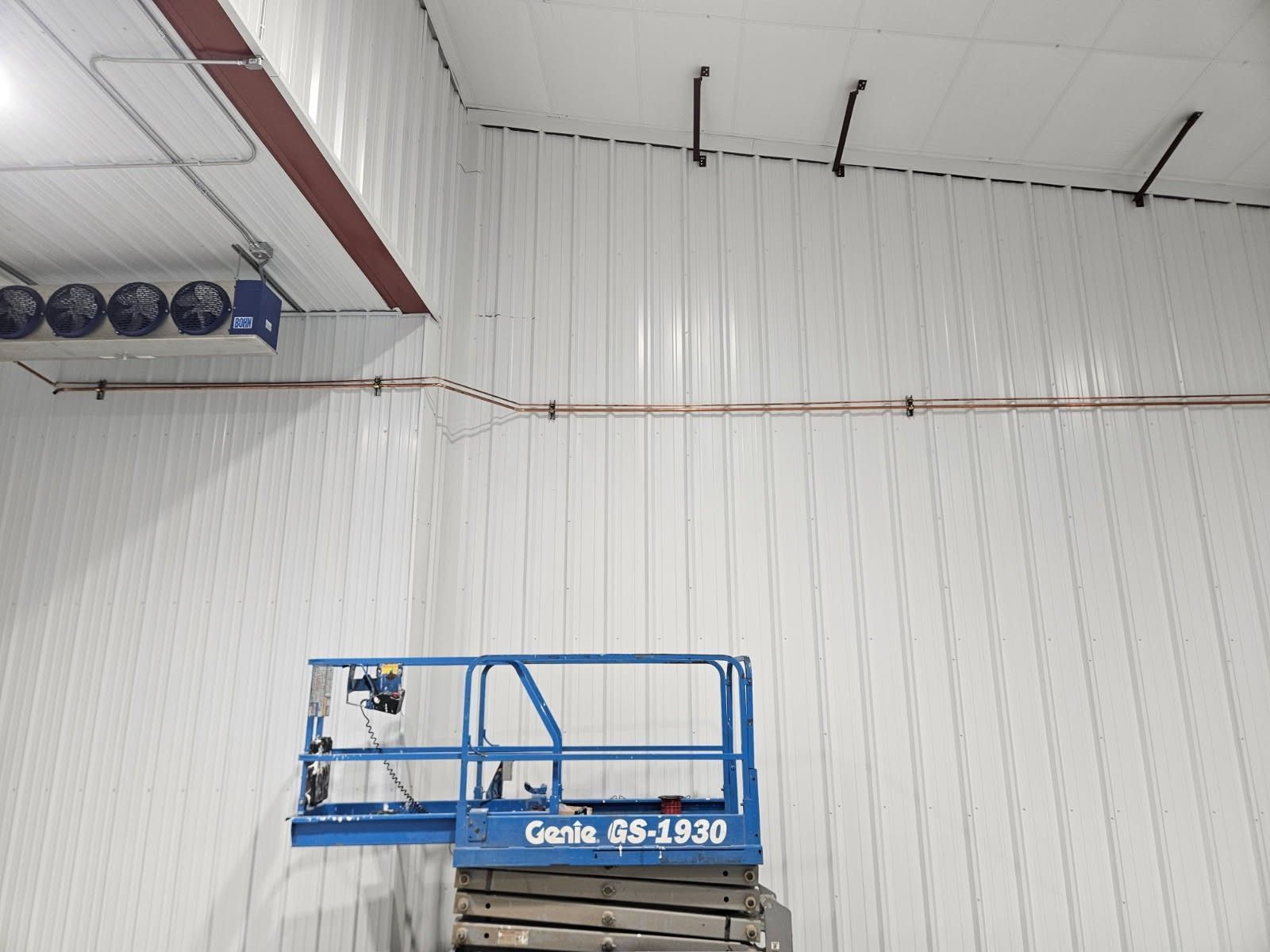 Blue scissor lift inside a large white industrial room with high walls and ceiling lights