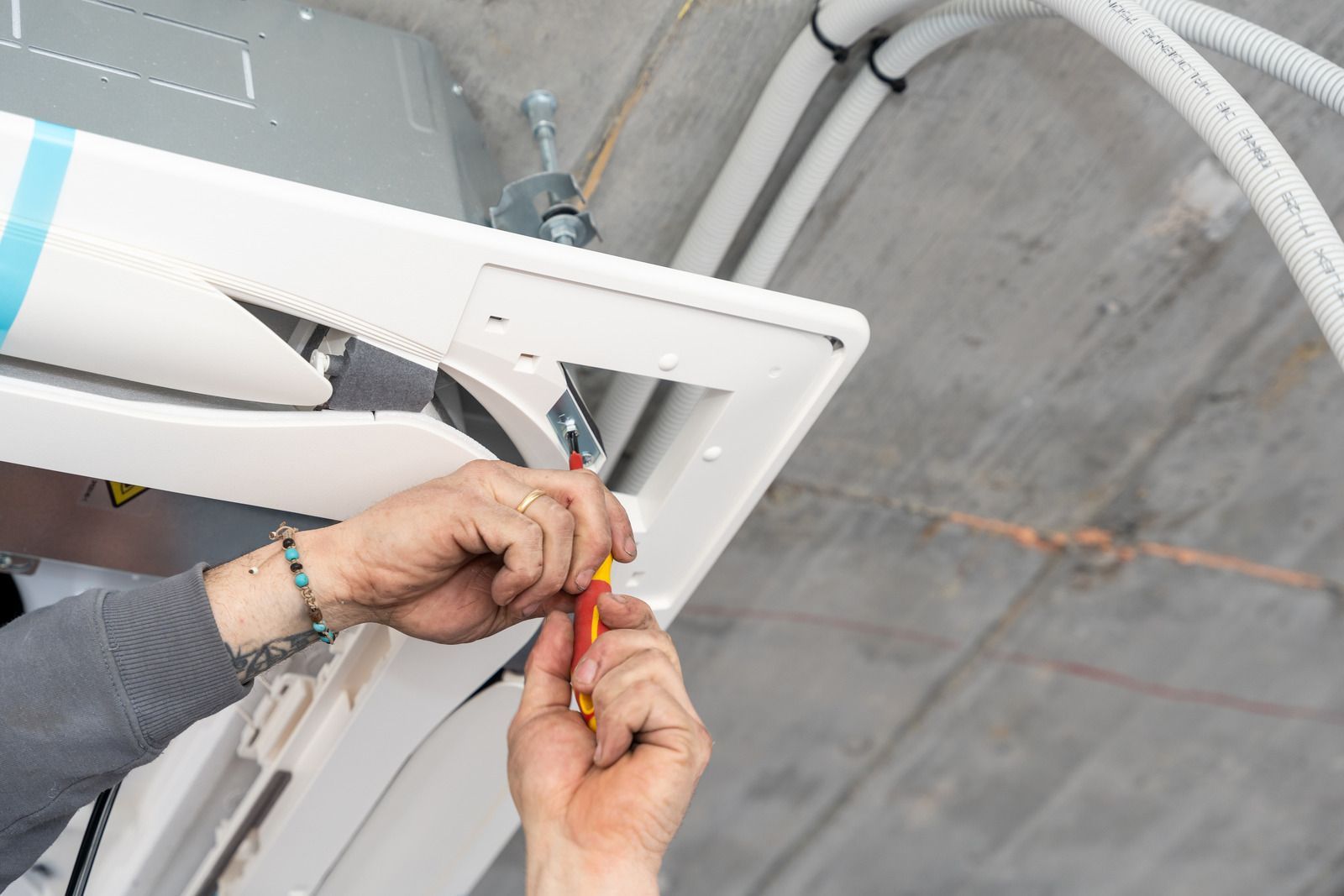 Hands using a screwdriver to install a white ceiling fixture on a concrete ceiling.