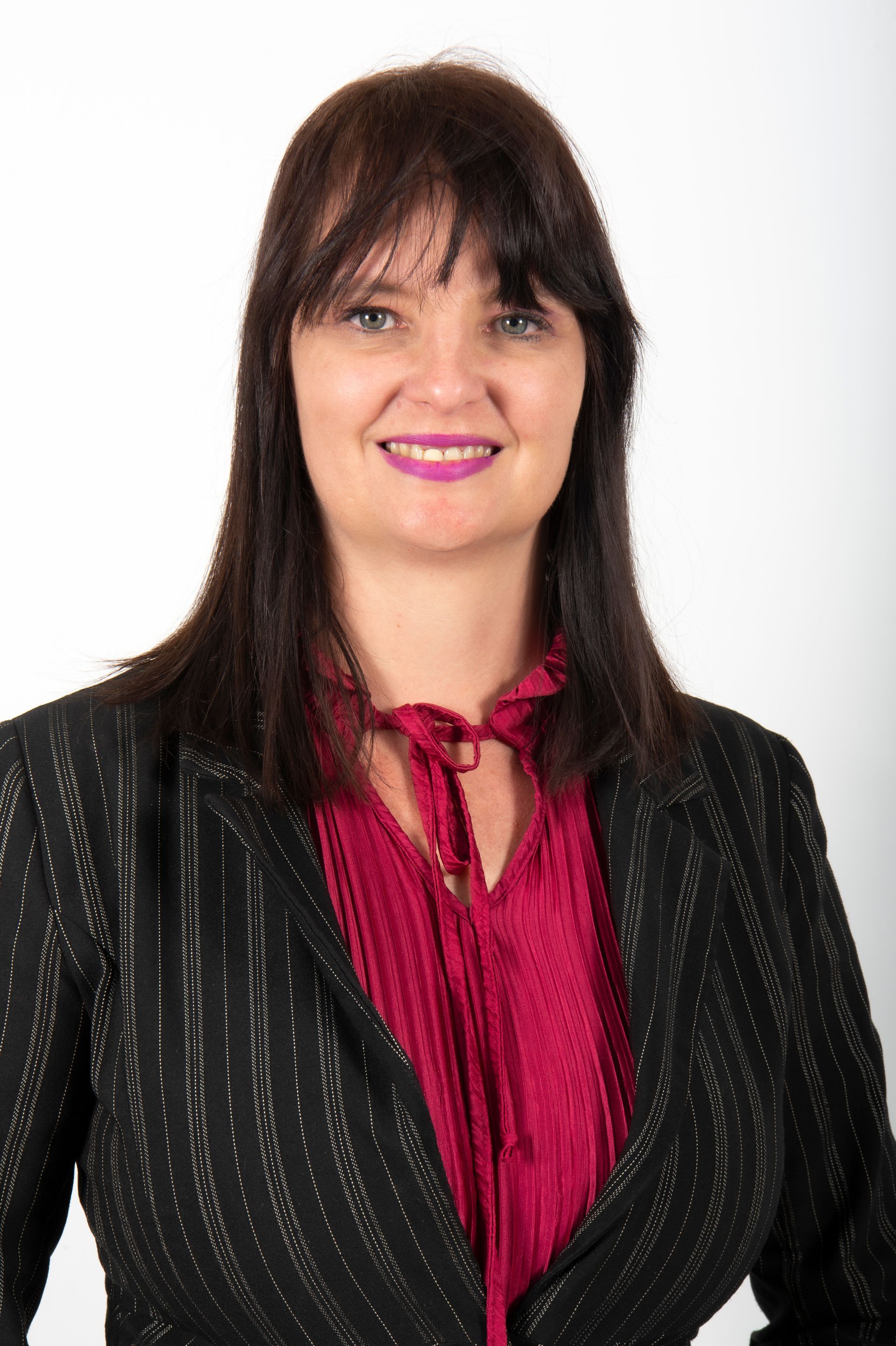 A woman wearing a black jacket and a red shirt is smiling for the camera.