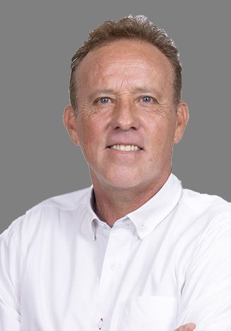 A man in a white shirt is smiling with his arms crossed.