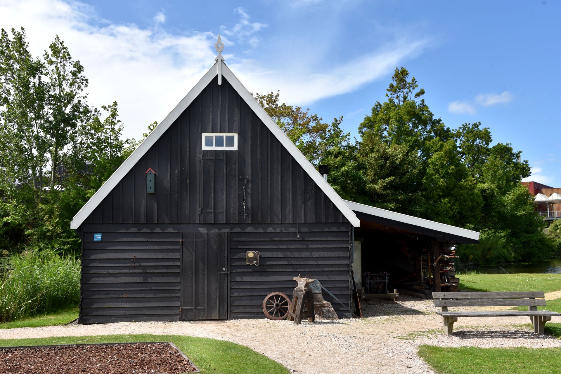A black barn with a white roof and a bench in front of it.