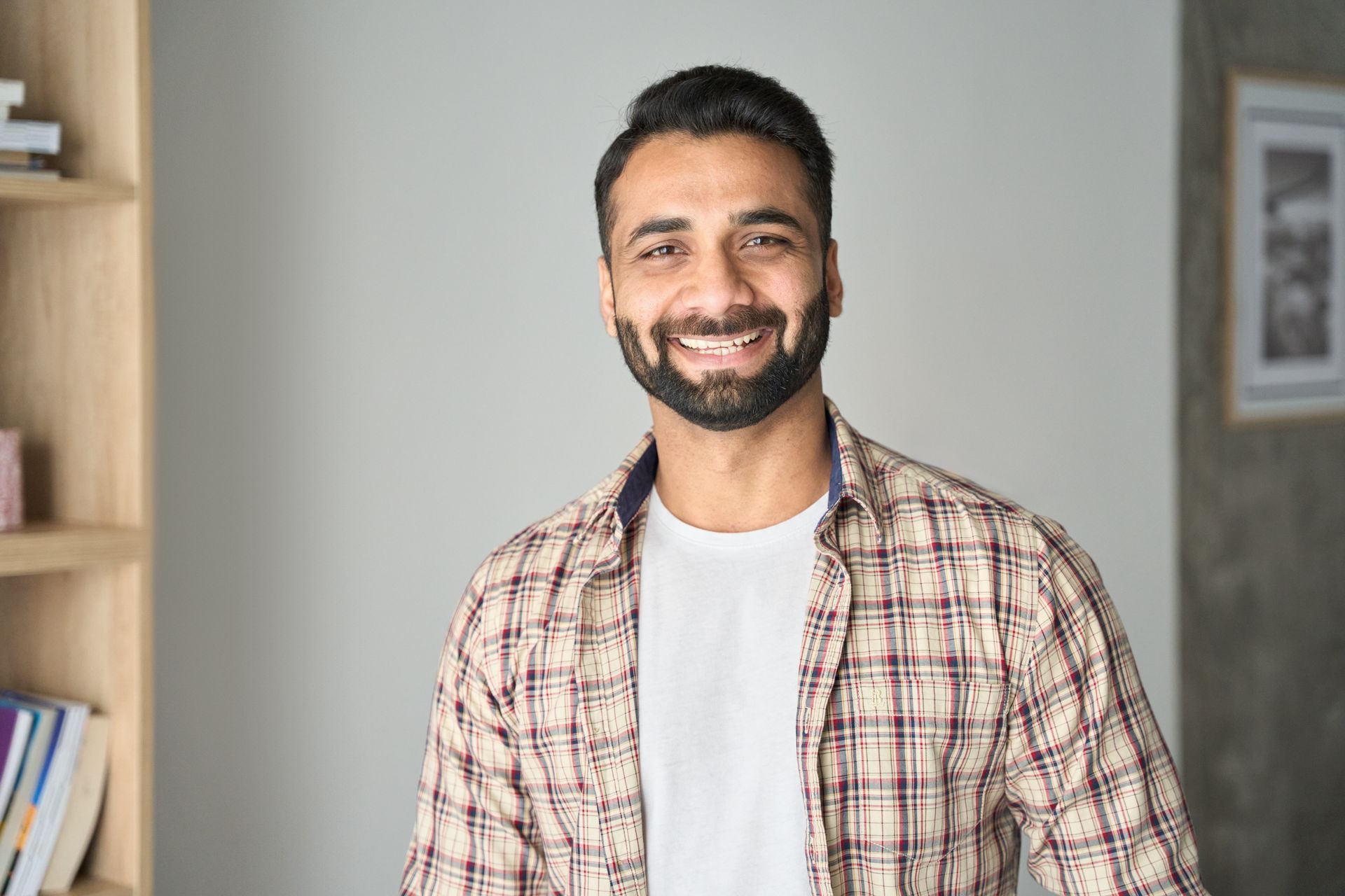 A man with a beard is smiling for the camera while wearing a plaid shirt.