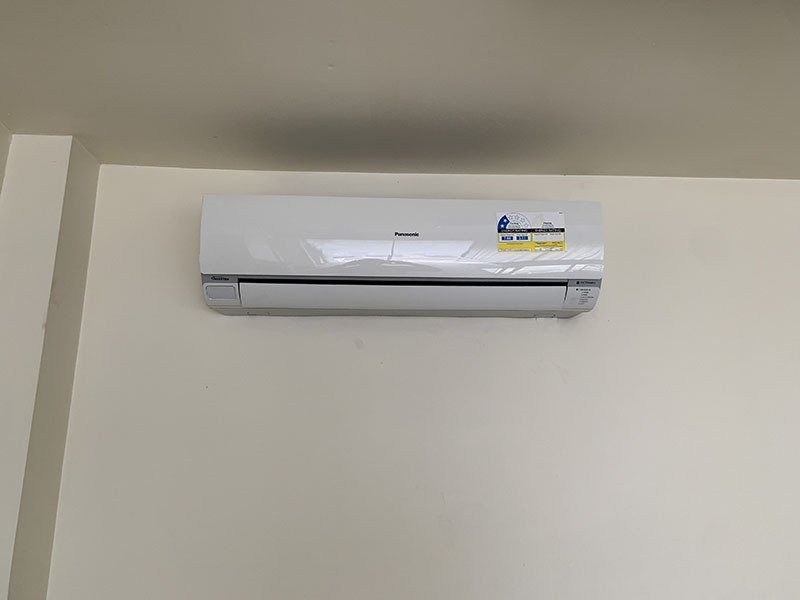 A White Air Conditioner is Hanging on a White Wall — Northside Air Conditioning Services In Ascot, QLD