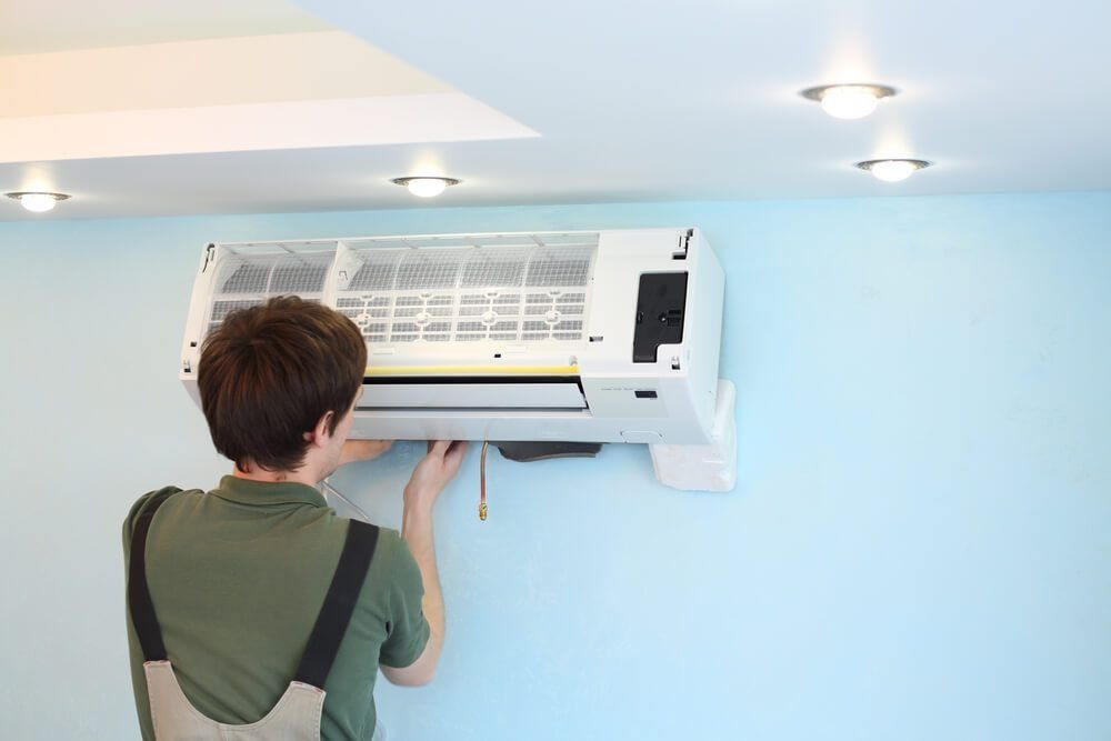 A Man is Installing an Air Conditioner on a Wall — Northside Air Conditioning Services In Ascot, QLD