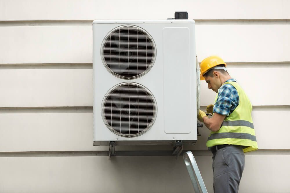 A Man is Installing an Air Conditioner on the Side of a Building — Northside Air Conditioning Services In Hendra, QLD