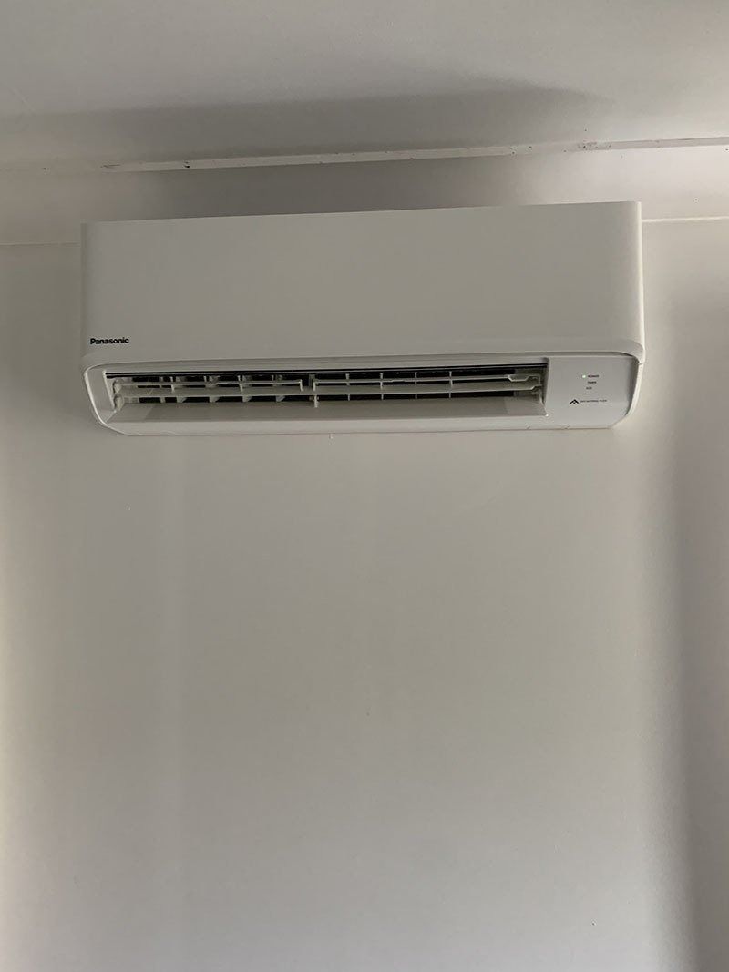 A White Air Conditioner is Hanging on a White Wall — Northside Air Conditioning Services In Aspley, QLD