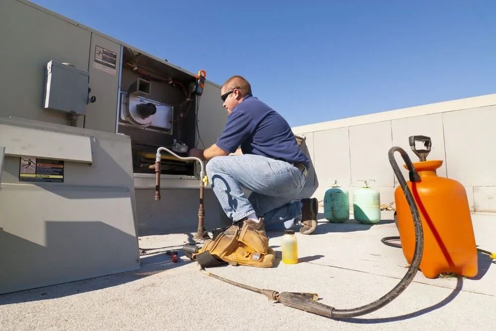 A Man is Working on an Air Conditioner on the Roof of a Building — Northside Air Conditioning Services In Hendra, QLD