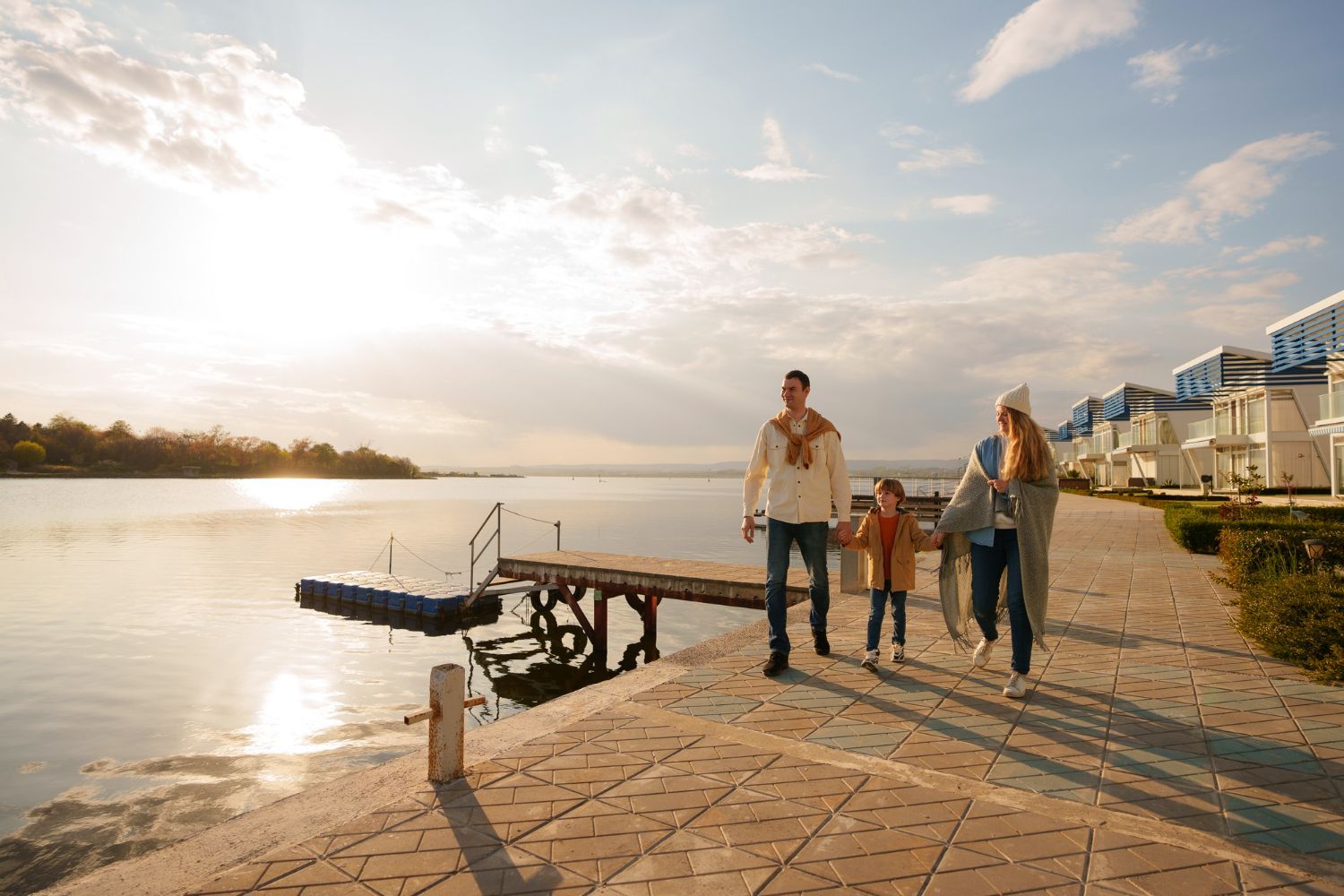 Family walking along a dock by a lake at sunset. The girl is holding hands with her parents.