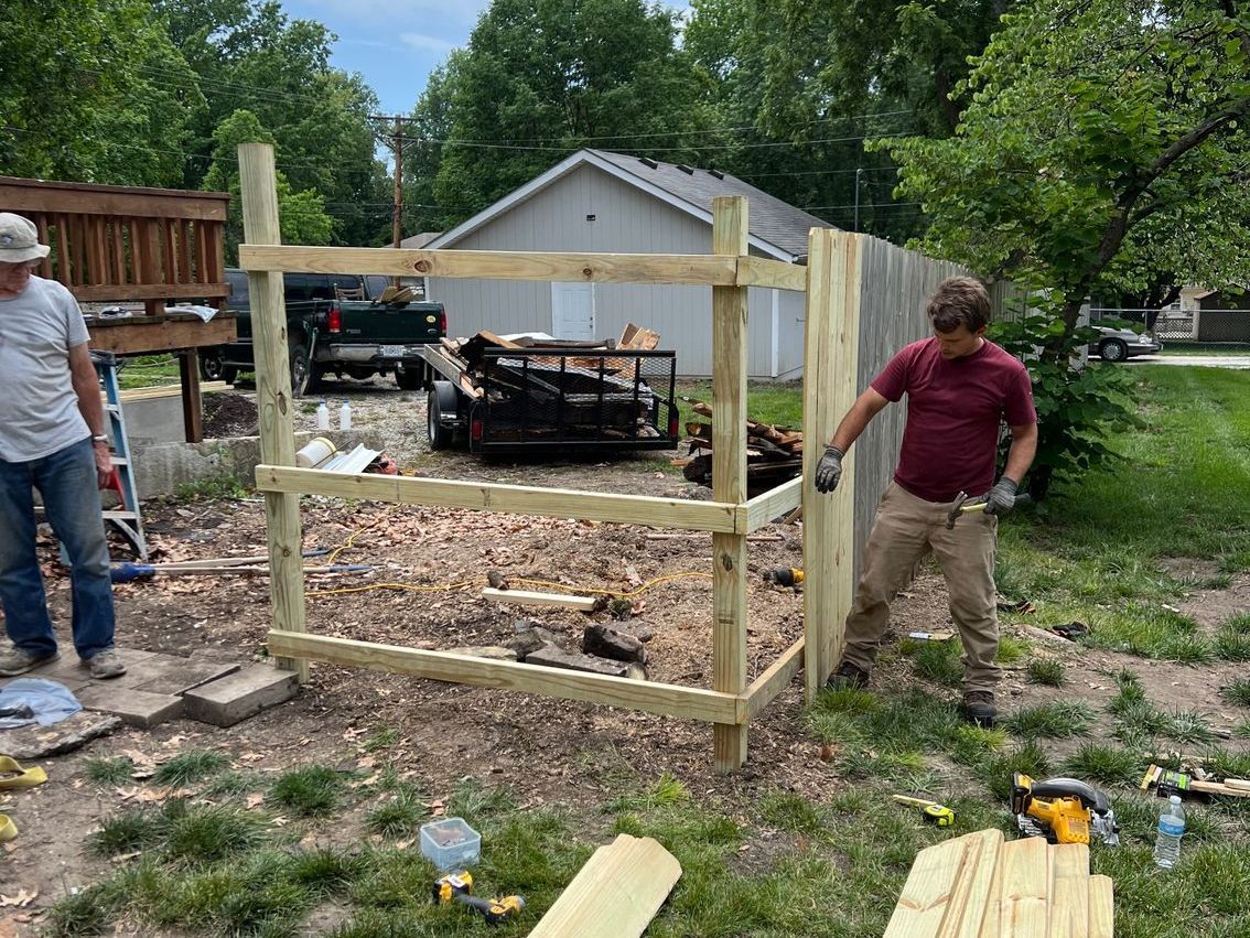 Eli Shipley and assistant building a wooden privacy fence in a yard beside a driveway and garage