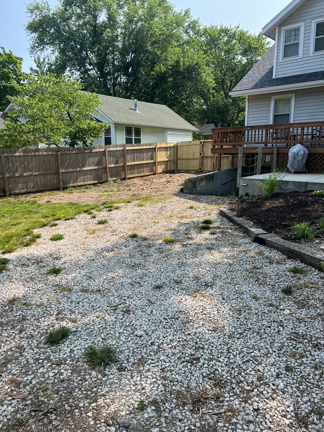 Newly installed wooden privacy fence, trees, white house and a deck with stairs on the right.